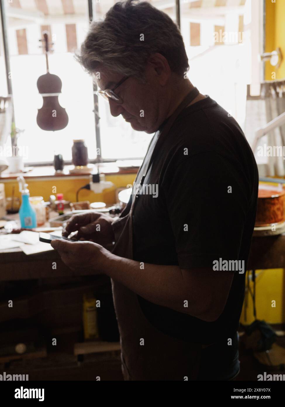 Silhouettenbauer mit Schwerpunkt auf Geigenbau in der gemütlichen Atmosphäre einer sonnendurchfluteten, holzgefüllten Handwerkstatt Stockfoto