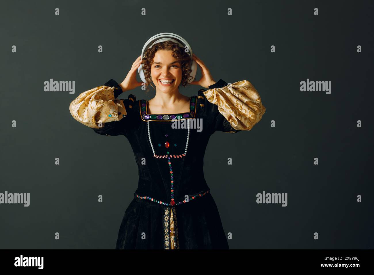 Porträt einer lächelnden Renaissance-Frau mit Kopfhörern und berührendem Kopf, in einem mittelalterlichen Kleid gekleidet, lauscht Musik Stockfoto