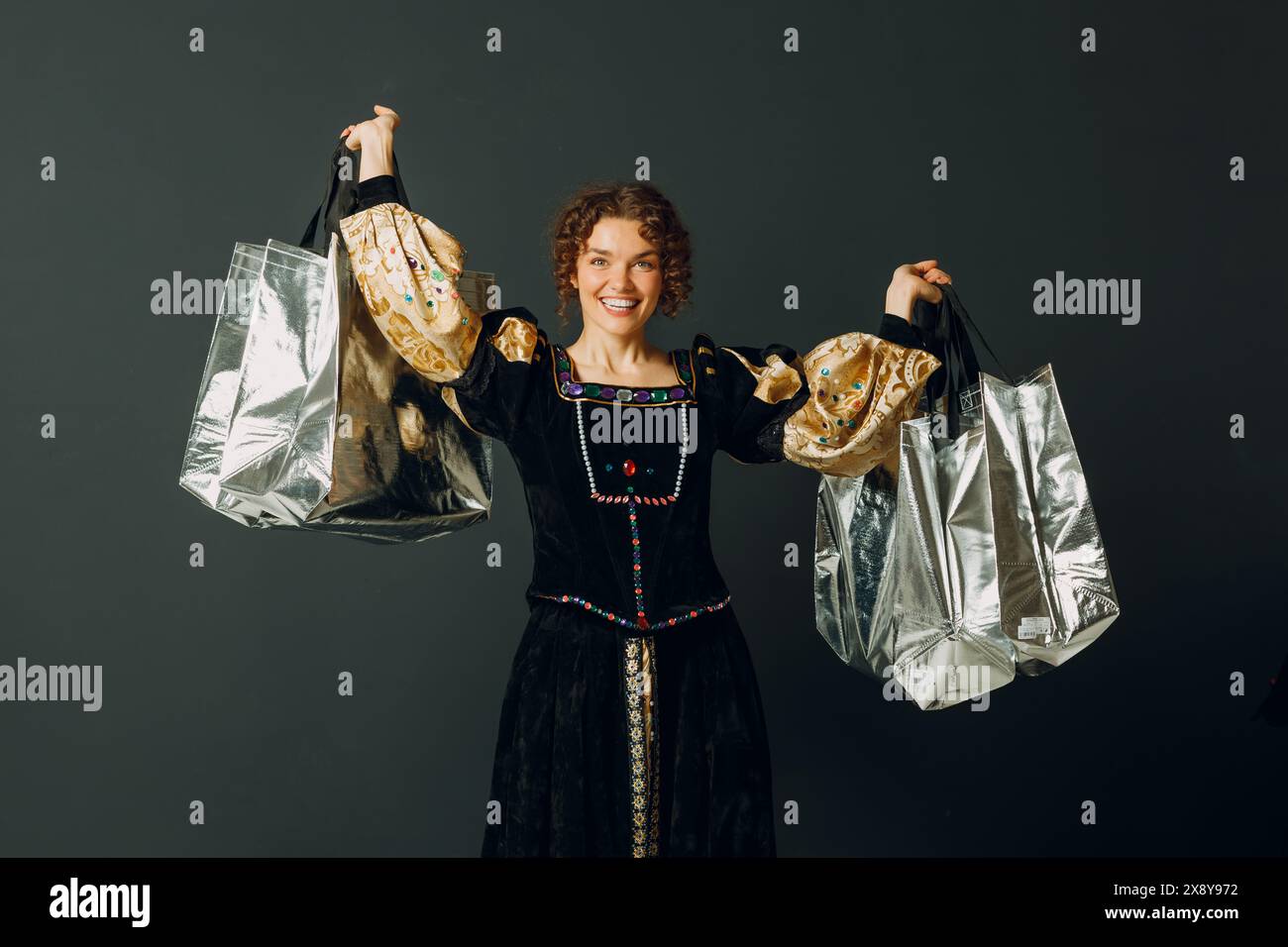 Porträt einer lächelnden jungen erwachsenen Frau in einem mittelalterlichen Kleid, die Einkaufstaschen in der Hand hält Stockfoto