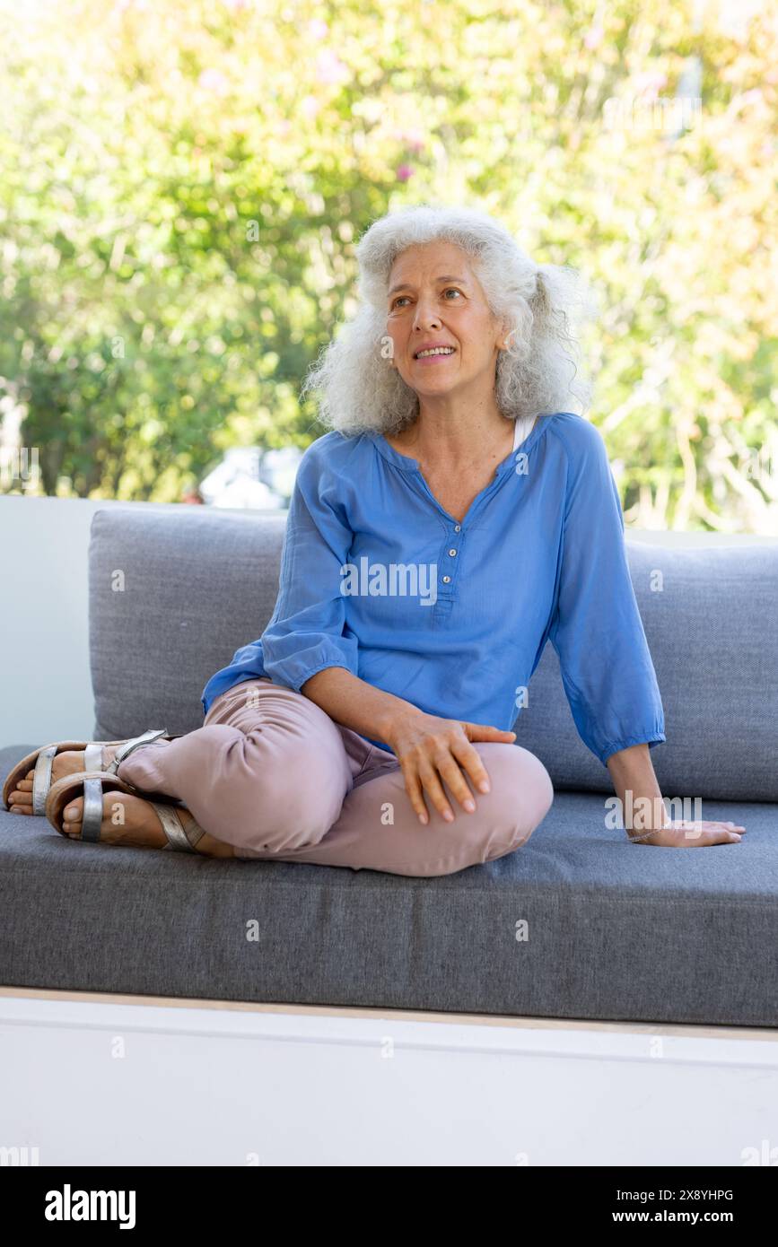 Draußen sitzt eine kaukasische Seniorin in blauem Hemd auf einem grauen Sofa Stockfoto