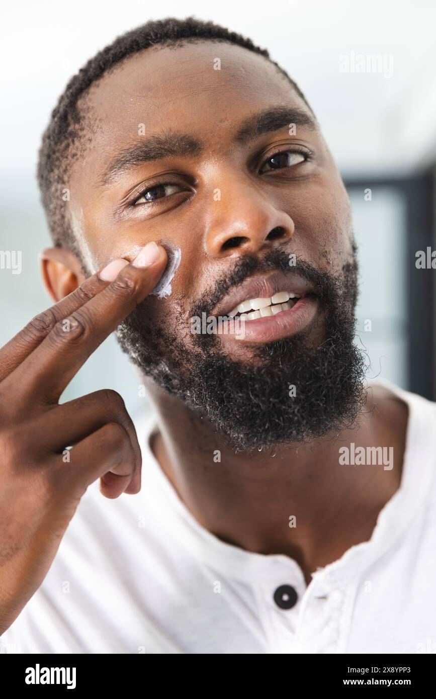 Zu Hause, Afroamerikaner, der Creme unter den Augen aufträgt Stockfoto
