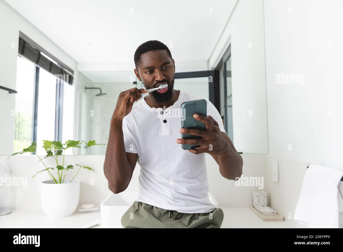 Zu Hause, Afroamerikaner, der Zähne putzt und das Telefon überprüft Stockfoto