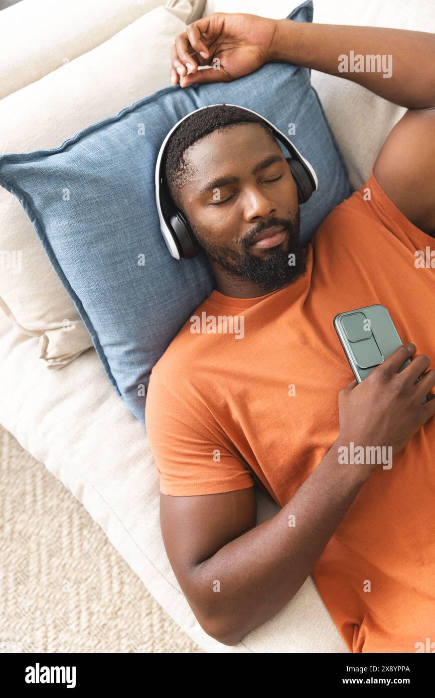 Der afroamerikanische Mann entspannt sich zu Hause mit Smartphone und Kopfhörern Stockfoto