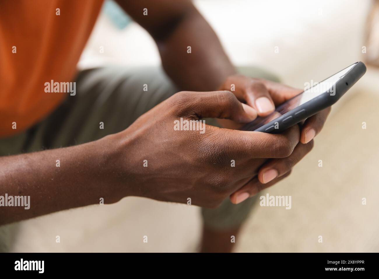 Zu Hause, Afroamerikaner Hausbesitzer mit Smartphone. Lässiges orangefarbenes Hemd mit dunklem Hintergrund Stockfoto