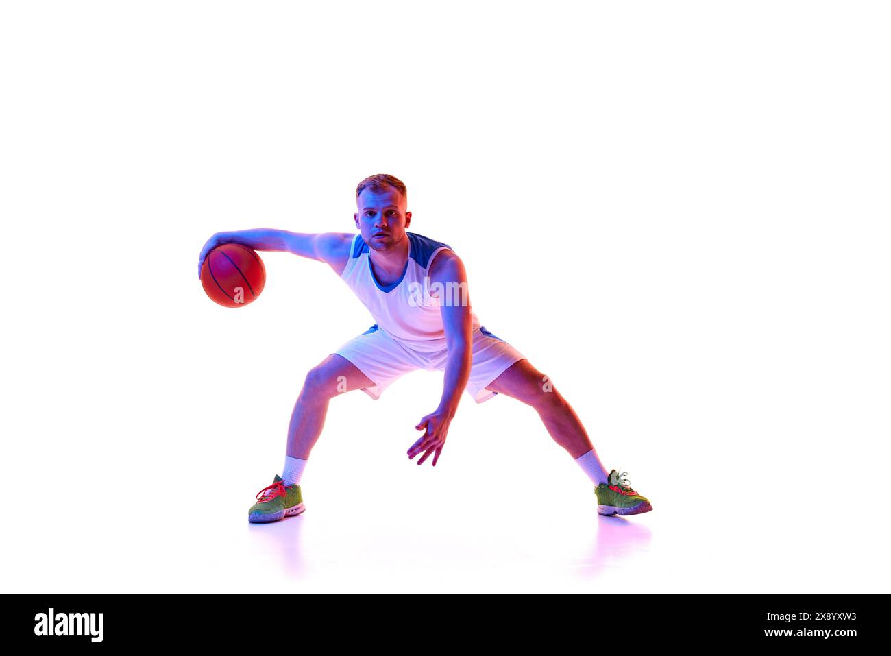 Dynamisches Porträt des jungen Athleten in roter Sportswear-Trainingsdribbeltechnik im Neonlicht vor weißem Studiohintergrund. Stockfoto