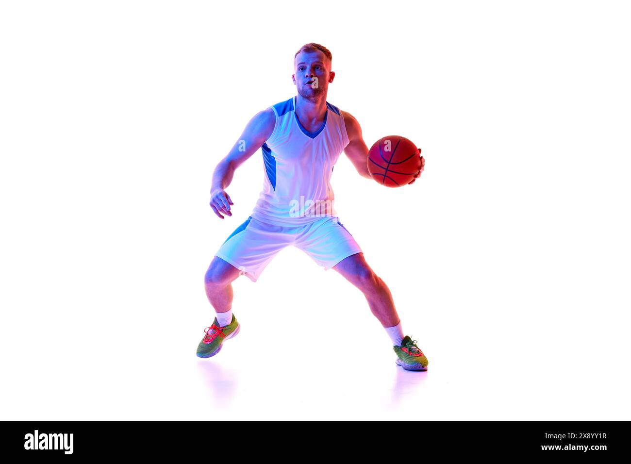 Junger athletischer Mann, professioneller Basketballspieler in roter Uniform, bereit, im Neonlicht vor weißem Studiohintergrund Tor zu schießen. Stockfoto