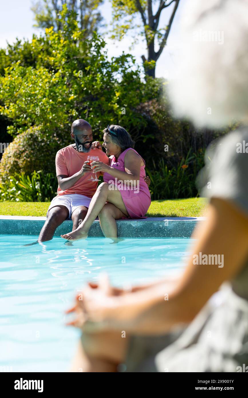 Im Freien, verschiedene Seniorenfreunde teilen sich Getränke am Pool und lachen zusammen Stockfoto