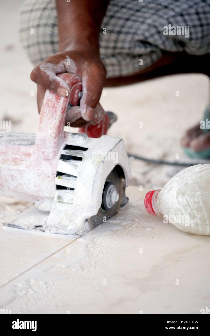 Eine detaillierte Nahaufnahme erfasst einen erfahrenen Handwerker, der mit einer handgeführten Motorsäge eine Fliese präzise schneidet, wobei Staub und Schmutz verstreut sind. Der Fokus Stockfoto