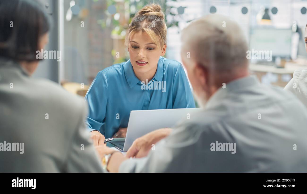 Im Konferenzraum diskutieren Unternehmer und Spezialisten am Konferenztisch über Statistiken und Diagramme, lösen Probleme, geleitet von weiblicher Teamleiterin. Sie verwenden Laptop Stockfoto