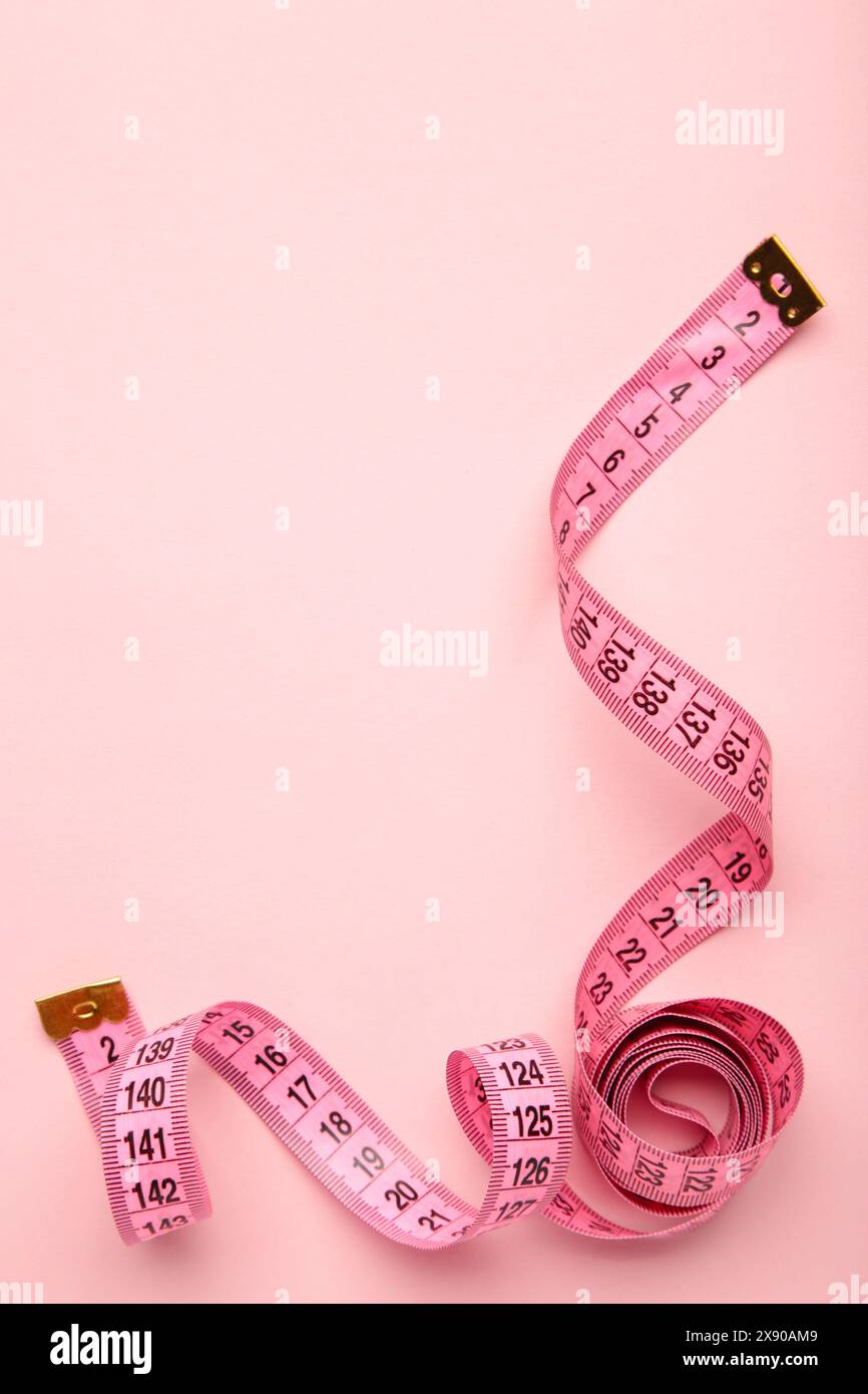 Rosafarbenes Kunststoff-Maßband mit metrischer Skala auf rosa Hintergrund. Draufsicht. Diätkonzept Stockfoto