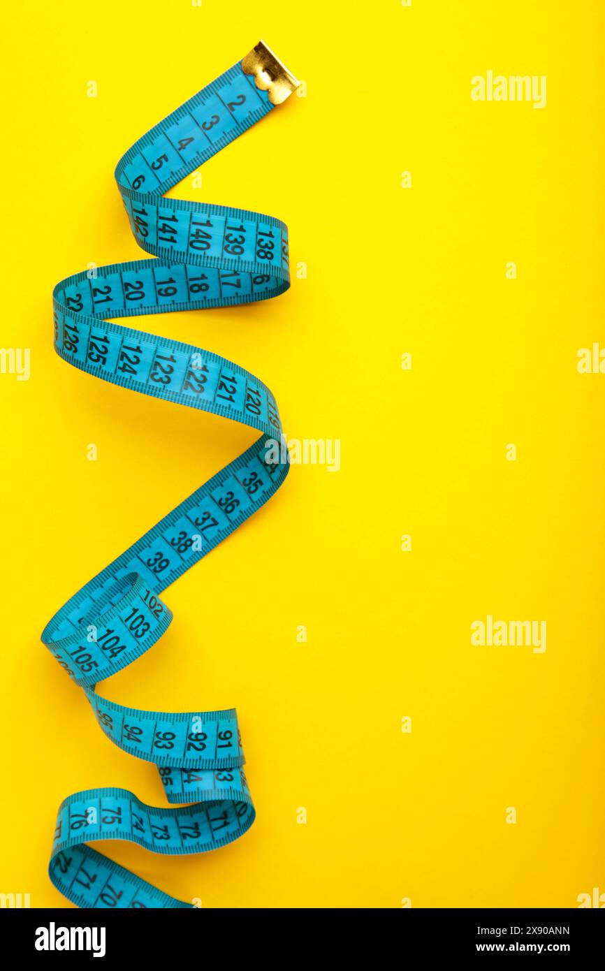 Blaues Kunststoff-Messband mit metrischer Skala auf gelbem Hintergrund. Draufsicht. Diätkonzept Stockfoto