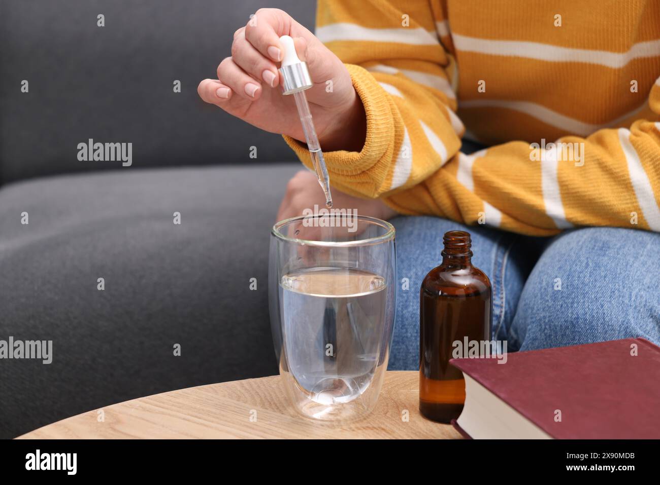 Frau tropft Nahrungsergänzungsmittel in Glas Wasser auf Holztisch drinnen, Nahaufnahme. Leerzeichen für Text Stockfoto
