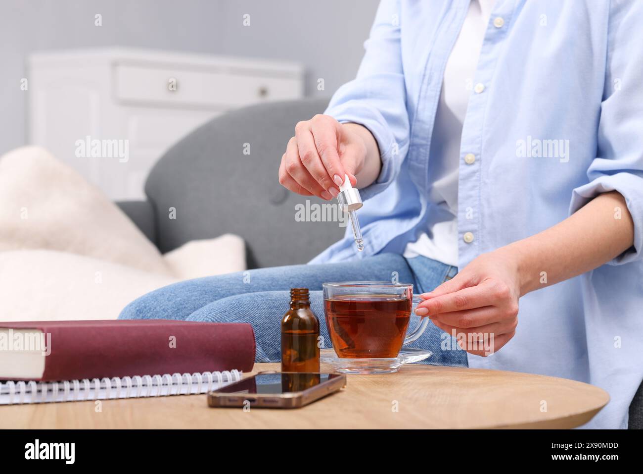 Frau tropft Nahrungsergänzungsmittel in eine Tasse Tee an einem Holztisch drinnen, Nahaufnahme Stockfoto