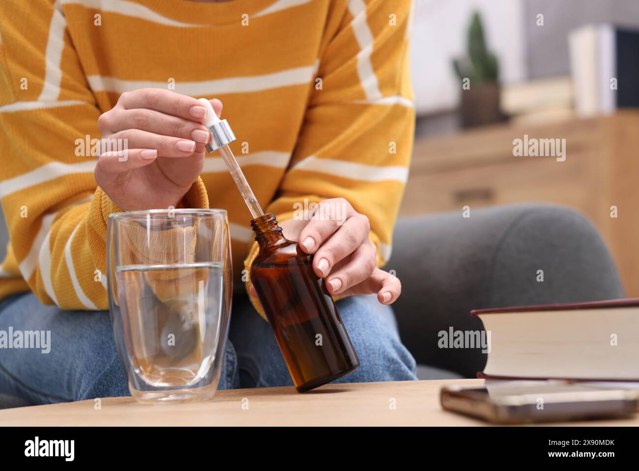 Frau tropft Nahrungsergänzungsmittel in Glas Wasser auf Holztisch drinnen, Nahaufnahme Stockfoto