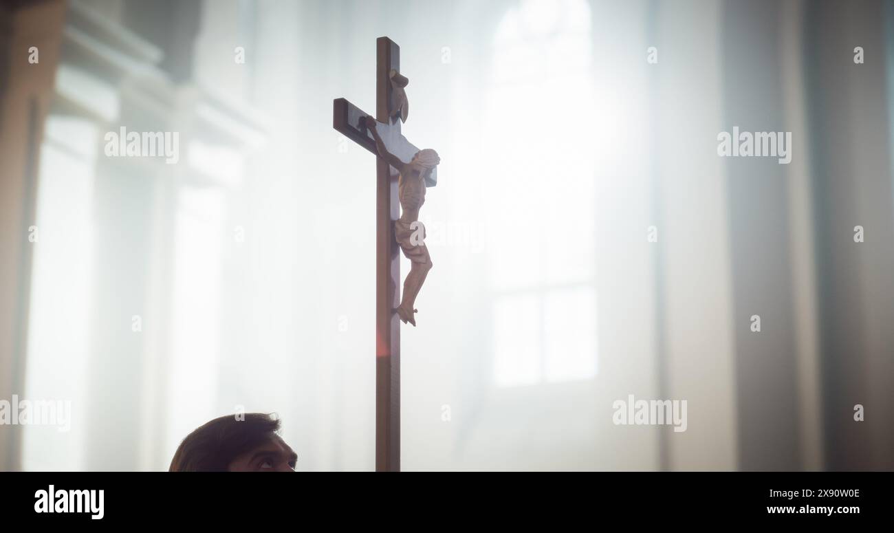 Nahaufnahme eines hölzernen Kreuzes mit der Statue der Kreuzigung Jesu Christi. Darstellung der Güte des Herrn und des Opfers für die Menschheit. Gottes Licht leuchtet auf ihn aus dem Fenster der Kirche Stockfoto