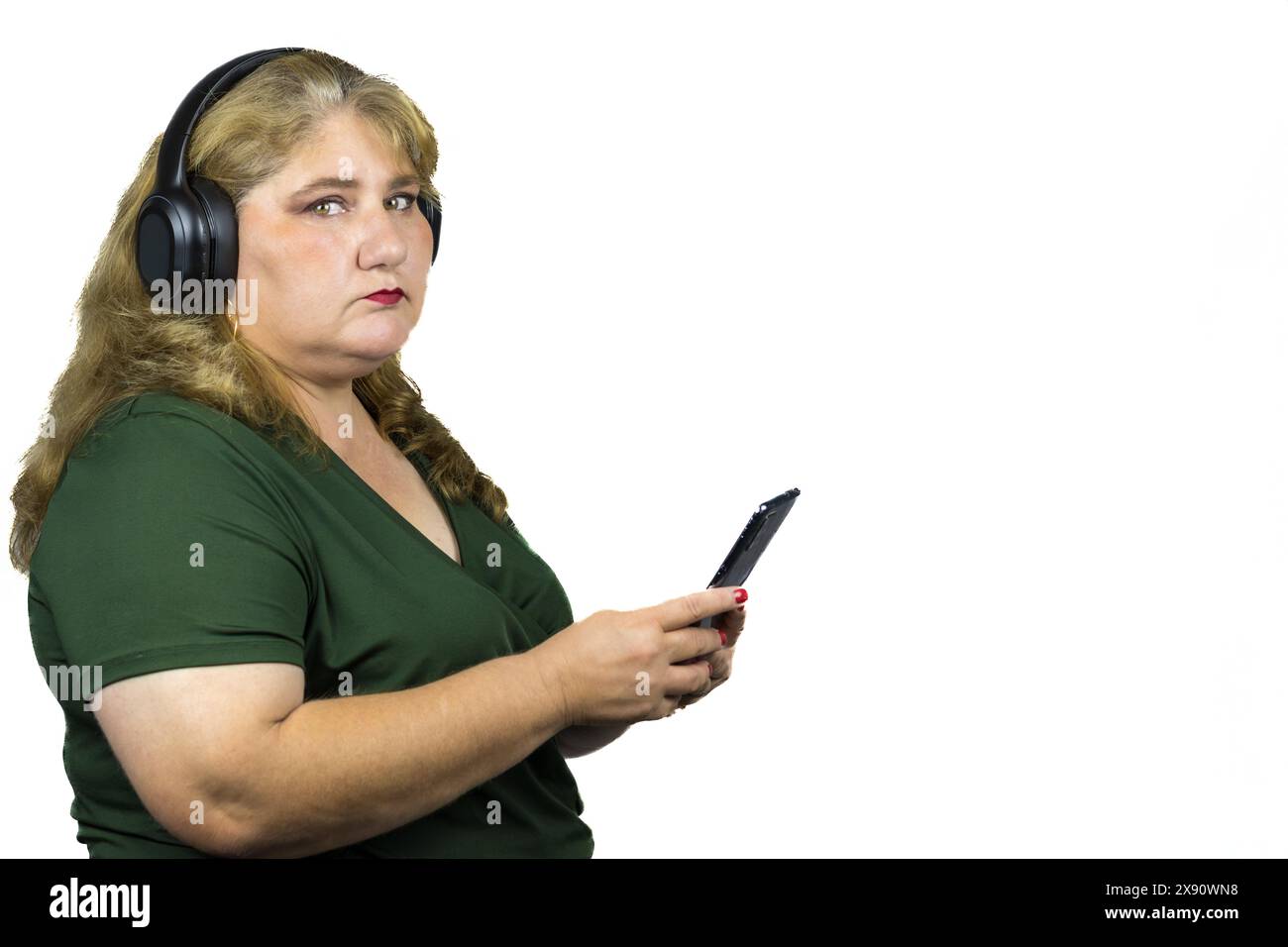 Weiße weiße Frau mittleren Alters mit leichter Fettleibigkeit, die über ihr Smartphone in die digitale Welt eingetaucht ist, während sie Bluetooth-Kopfhörer trägt. Stockfoto