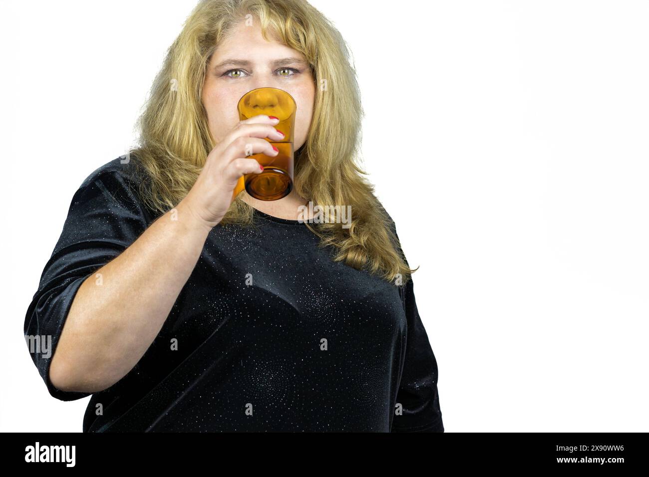 Dieses Bild fängt den ruhigen Moment einer 50-jährigen blonden Frau mit auffälligen grünen Augen ein, die ein erfrischendes Glas Wasser genießt. Stockfoto