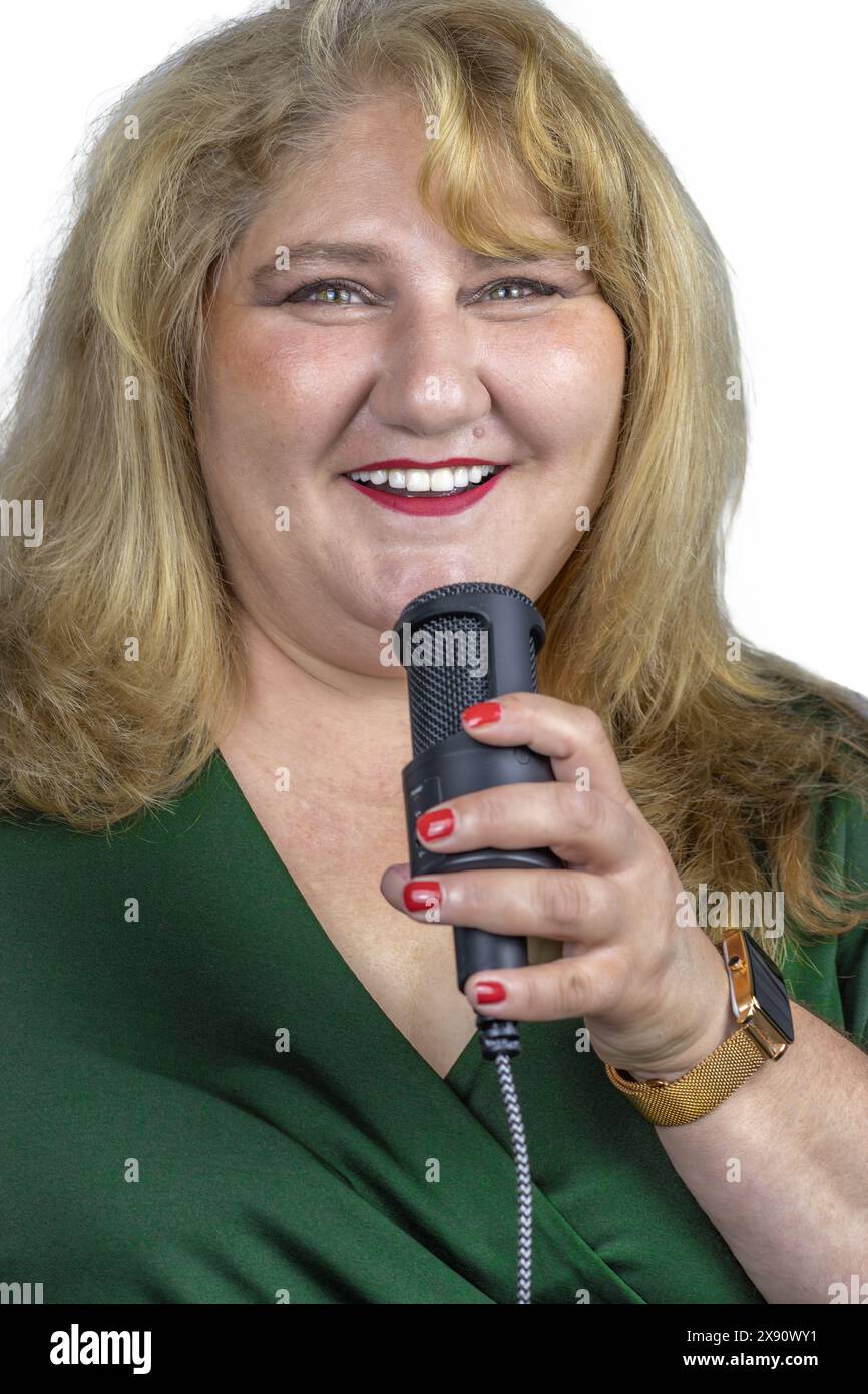 Dieses Bild fängt einen fröhlichen Moment einer 50-jährigen weißen Frau mit blonden Haaren ein, hält ein Mikrofon und lächelt. Ihr strahlendes Lächeln und t Stockfoto