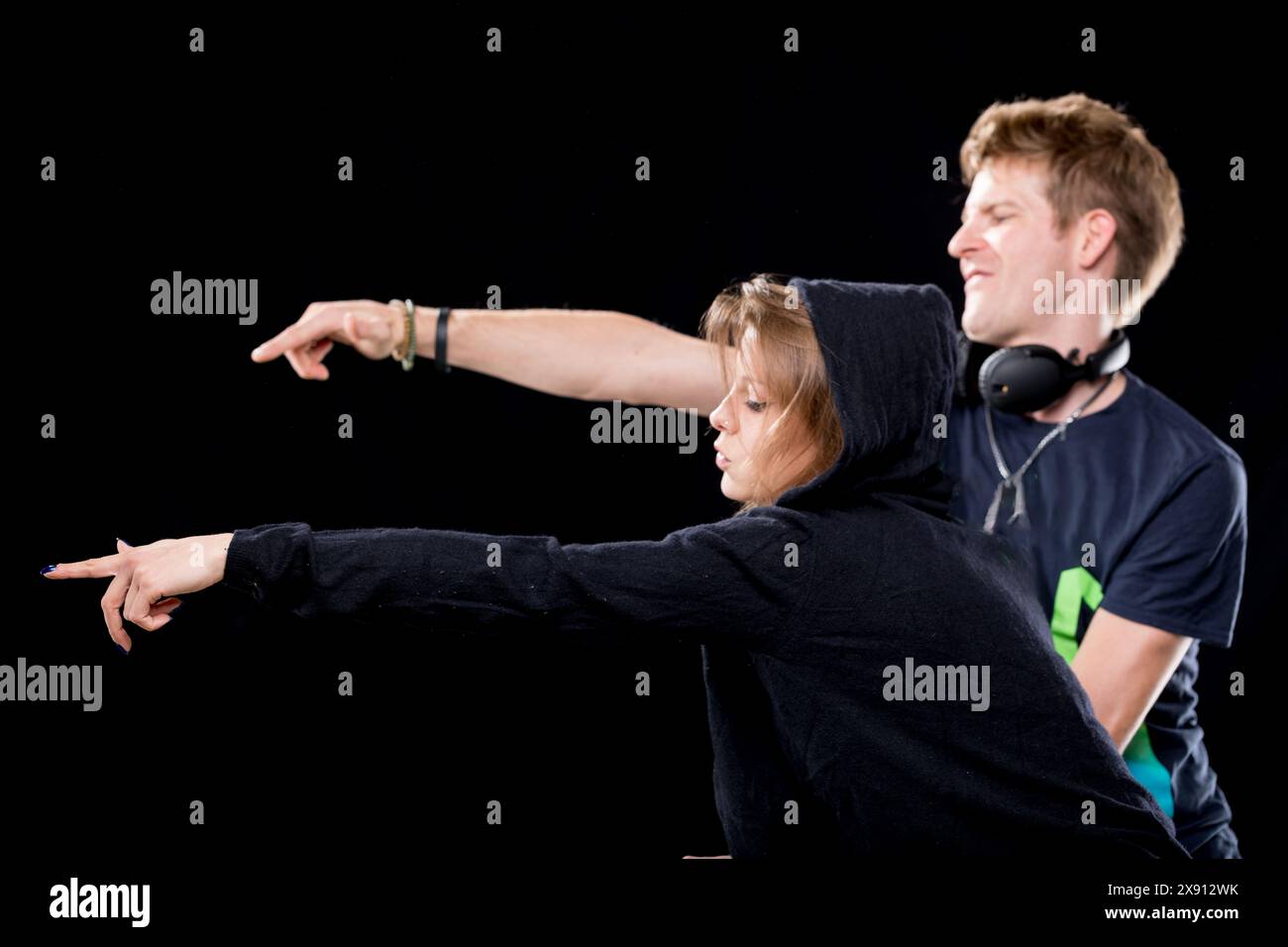 Zwei lässig gekleidete DJs interagieren energetisch, während sie am Mixer arbeiten. Die Frau in einem Kapuzenpulli lächelt breit und der Mann zeigt Begeisterung Stockfoto