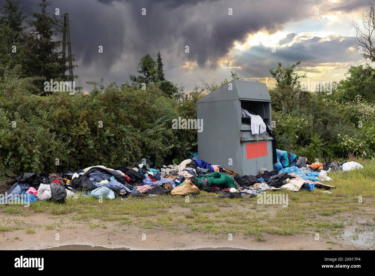 Bekleidungsabfälle in der Natur. Weggeworfene Kleidung durch Spendenbehälter. Stockfoto