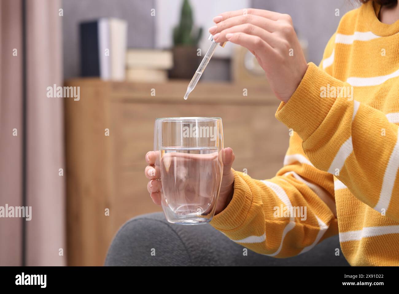 Frau tropft Nahrungsergänzungsmittel in Glas Wasser drinnen, Nahaufnahme Stockfoto
