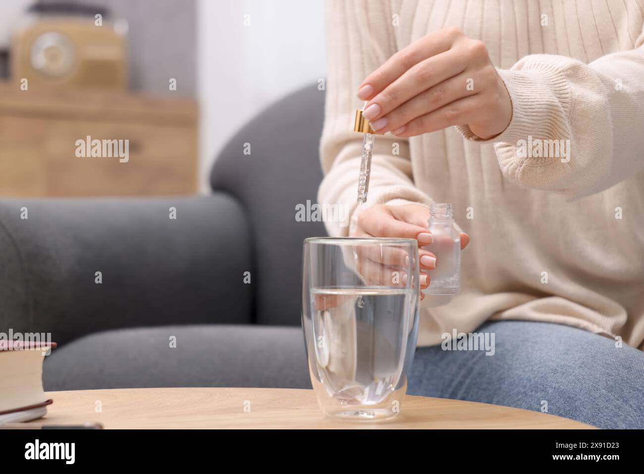 Frau tropft Nahrungsergänzungsmittel in Glas Wasser auf Holztisch drinnen, Nahaufnahme. Leerzeichen für Text Stockfoto