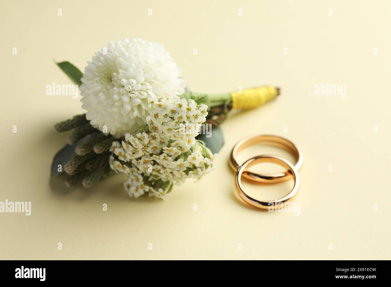 Kleine stilvolle Boutonniere und Ringe auf beigefarbenem Hintergrund Stockfoto
