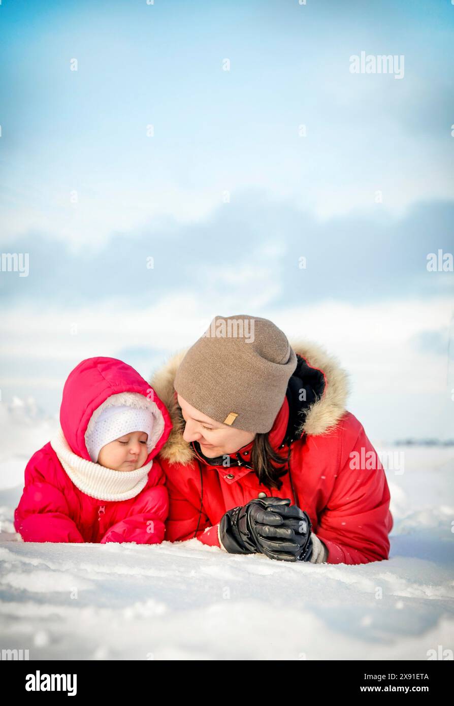 Mutter und Kind in roten Jacken genießen das schneebedeckte Winterwetter, liegen auf dem Schnee und lächeln einander an, Weißrussland, Minsk Stockfoto