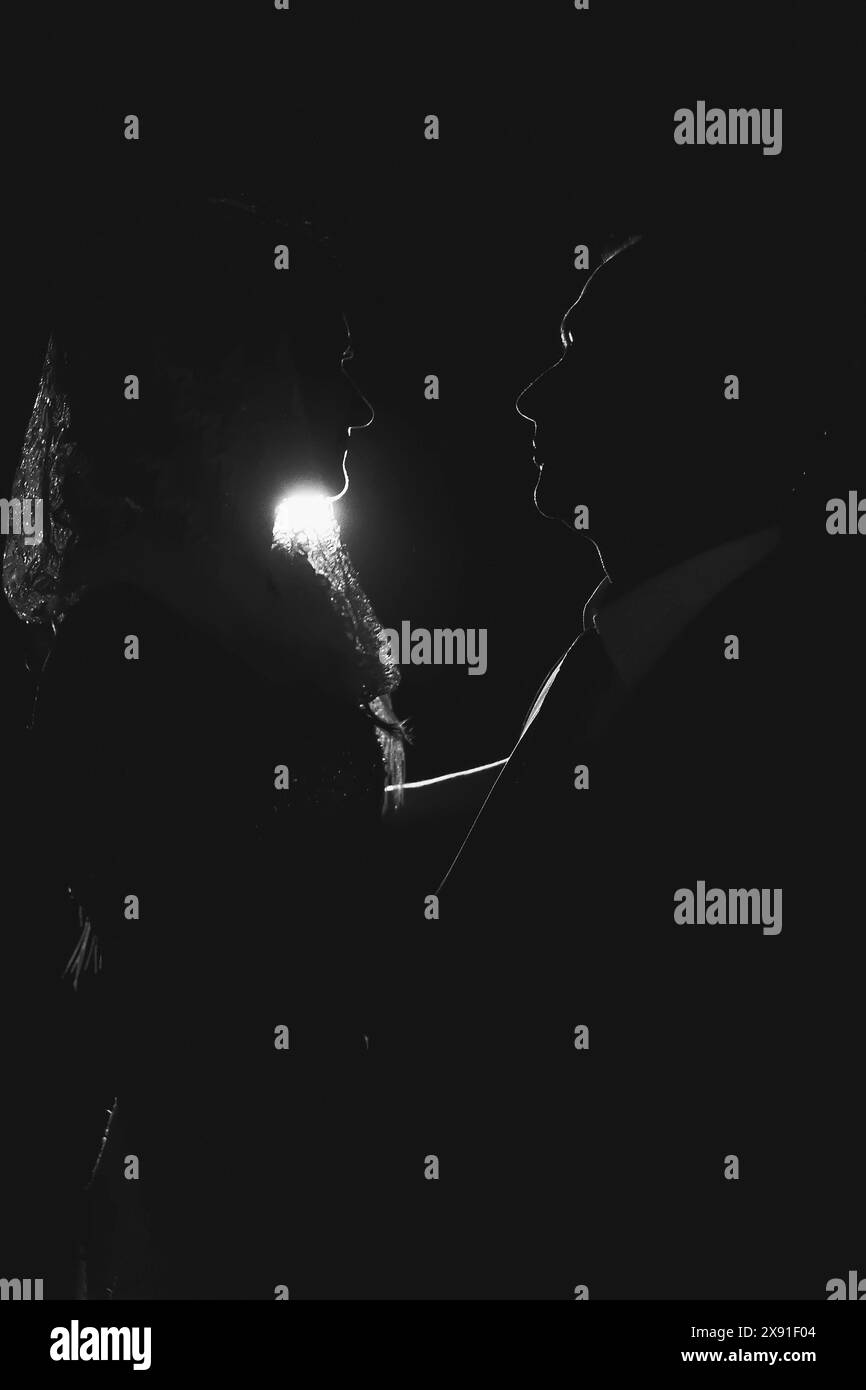 Silhouette einer Braut und eines Bräutigams in einem intimen Moment mit dramatischer Beleuchtung in einer dunklen Umgebung Stockfoto
