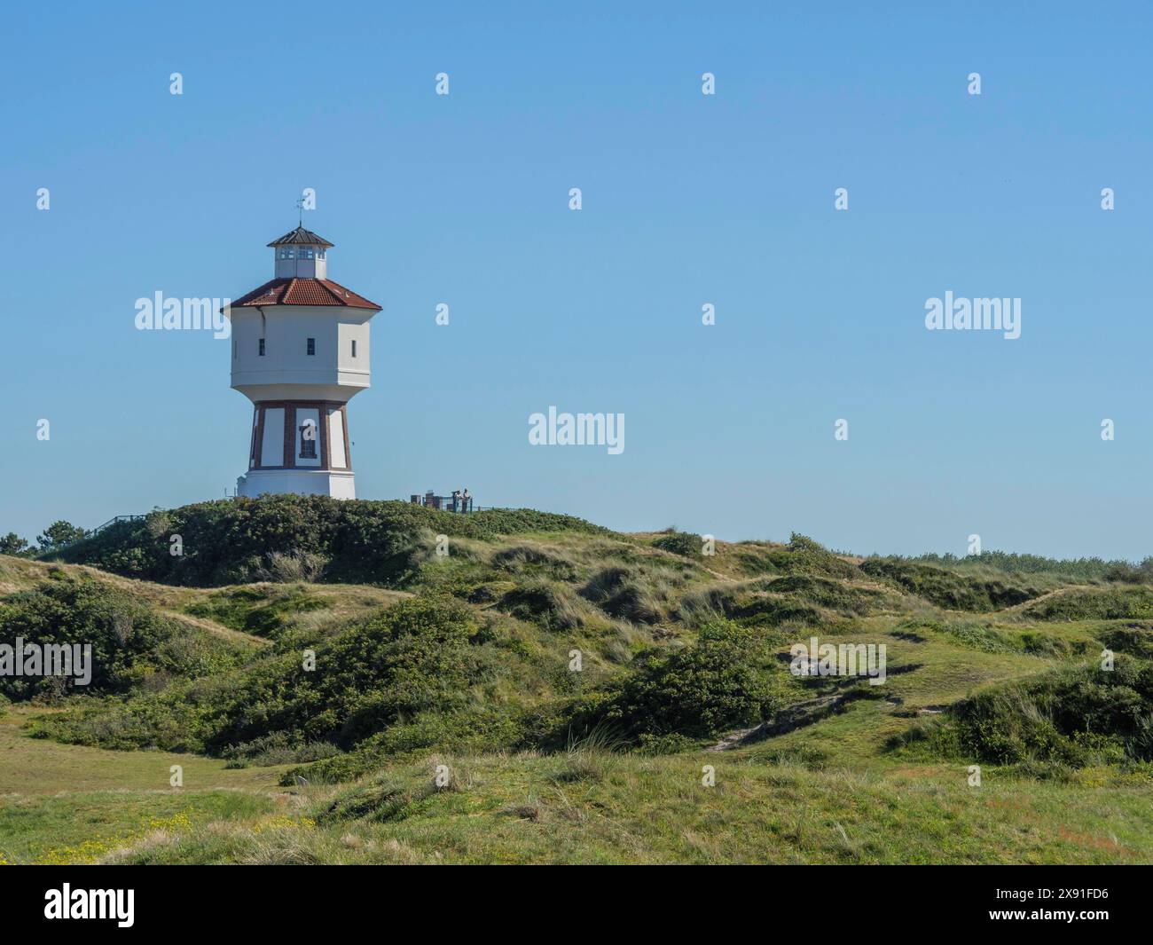 Ein Leuchtturm steht auf einem grasbewachsenen Hügel unter blauem Himmel, die Atmosphäre ist friedlich und ruhig, Wasserturm in den Dünen einer Insel, langeoog, deutschland Stockfoto