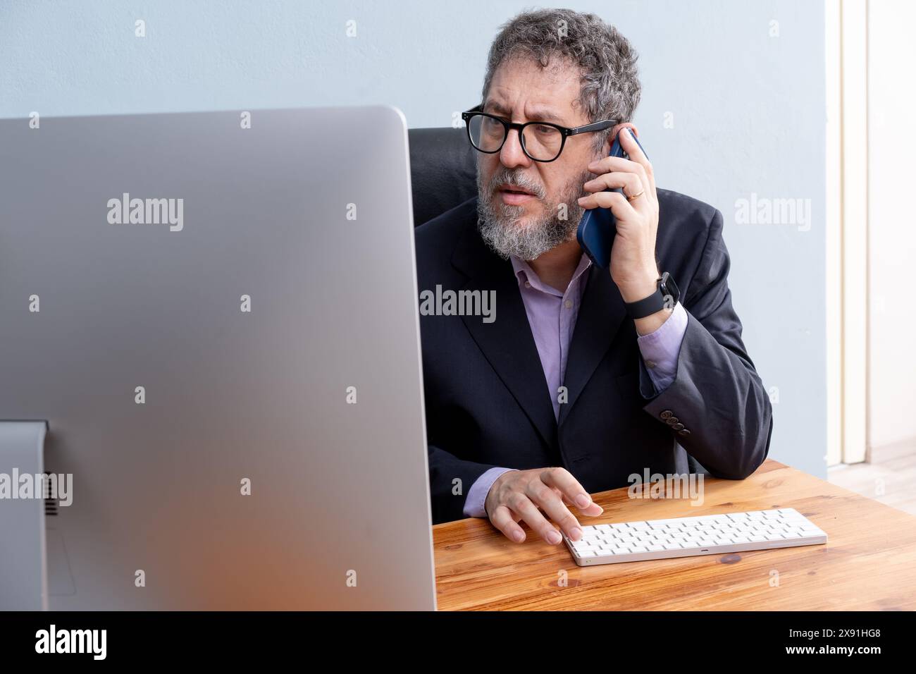 Professioneller Geschäftsmann, der am Telefon telefoniert, während er an einem Computer in seinem Büro arbeitet – Unternehmenskommunikation, Professionalität und effiziente Arbeit Stockfoto