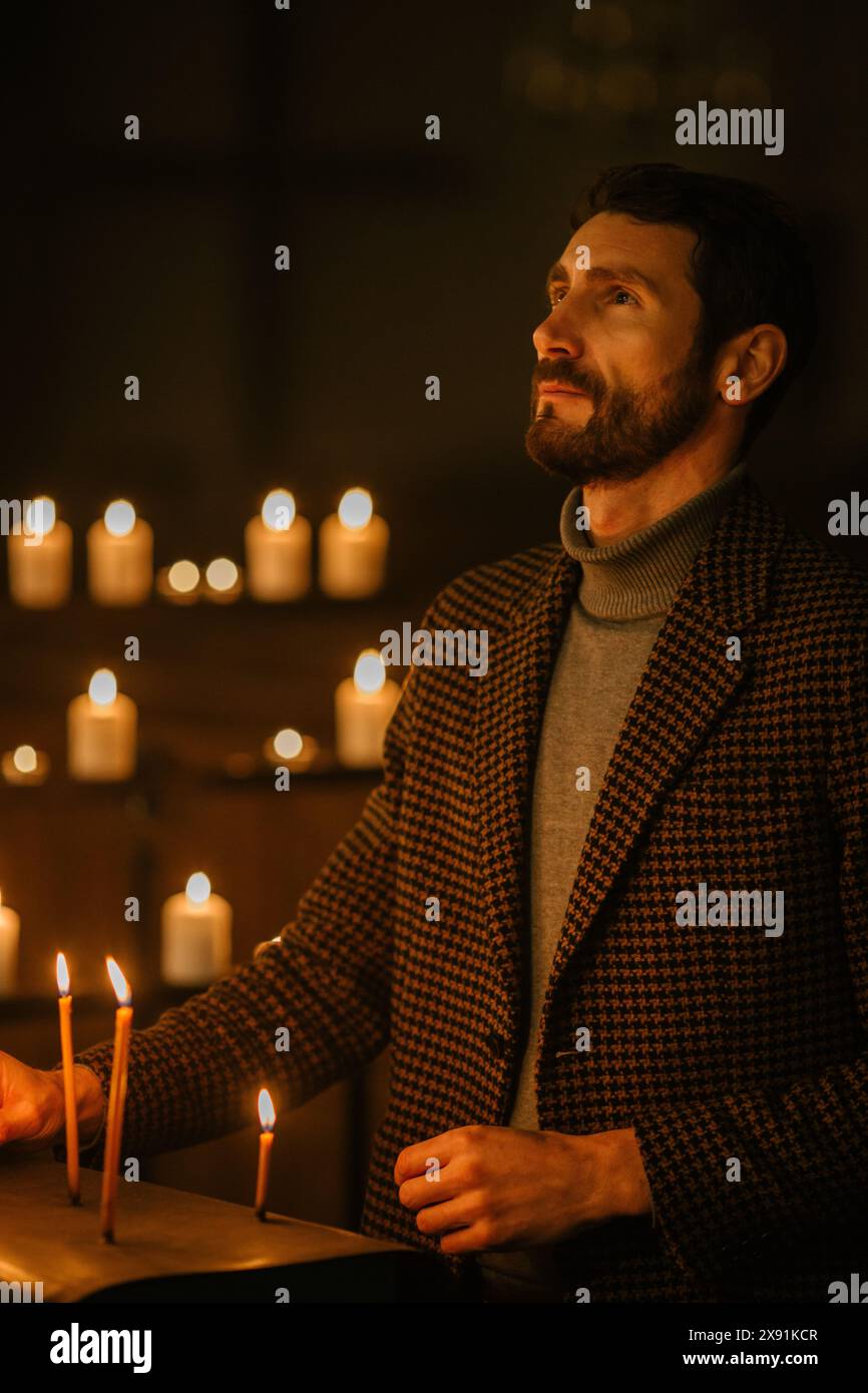 Fromme christliche Mann zündet eine Kerze in der Kirche an, betet und drückt die Hingabe zu Gott aus. Akt des Glaubens und der Hoffnung. Symbolisiert das Licht der Lehre Jesu Christi von ewiger Liebe und Barmherzigkeit Stockfoto