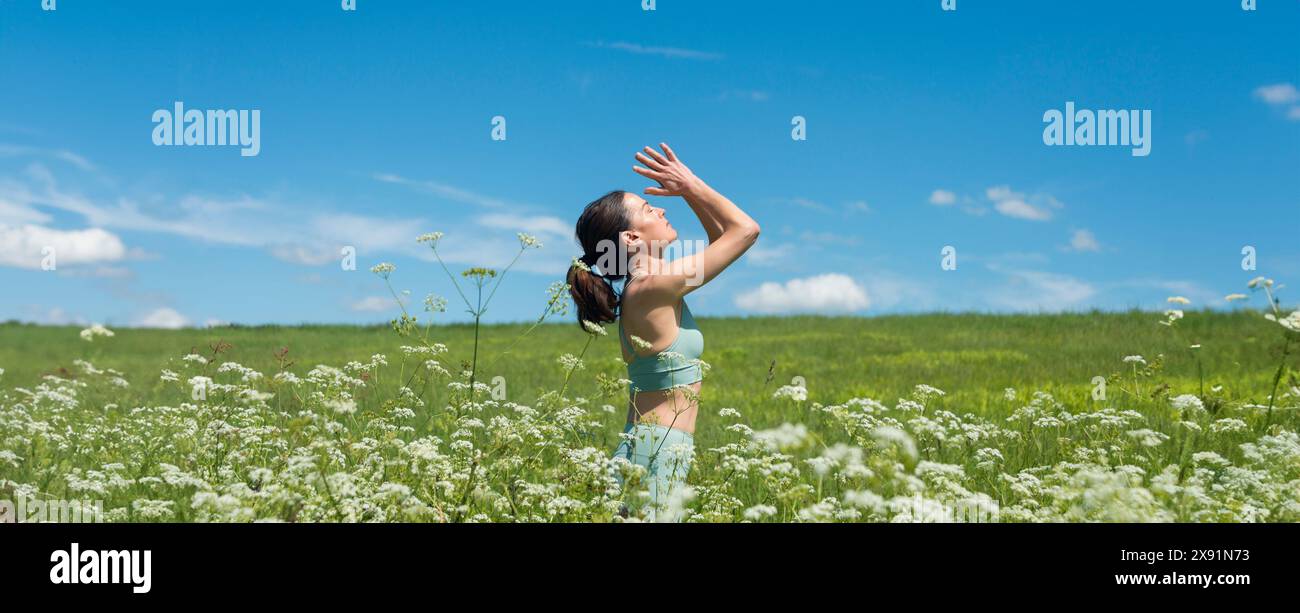 Frau, die in einem Feld voller wilder Blumen steht, meditiert und tief atmet, Yoga draußen. Stockfoto