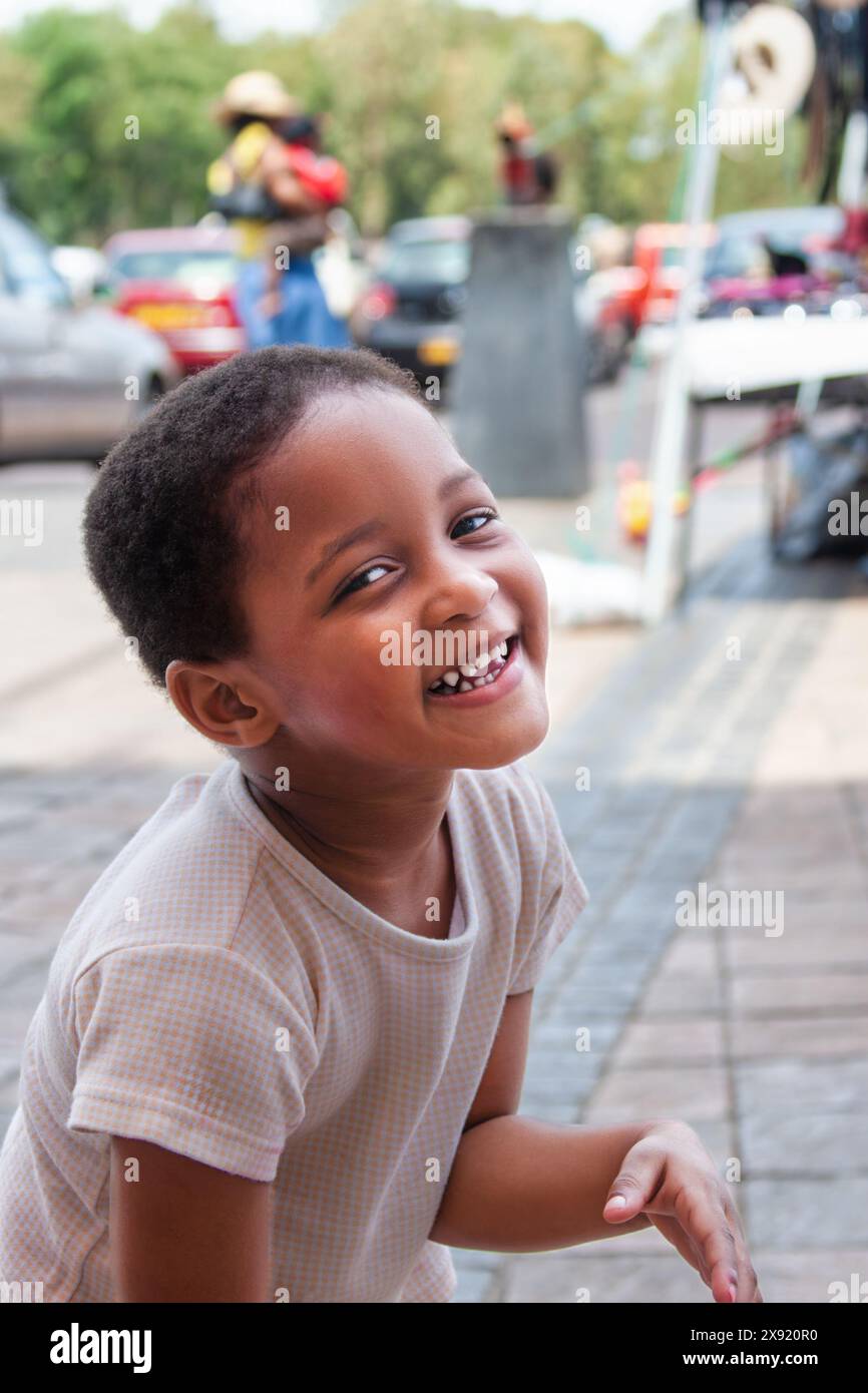 Kopffoto eines glücklichen afrikanischen Mädchens draußen, das auf der Straße steht, in einem Einkaufszentrum mit Autos parkt Stockfoto