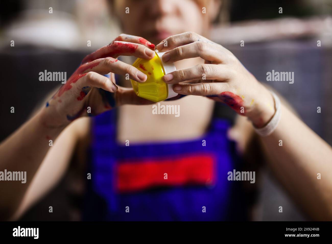 Nahaufnahme der Hände einer Künstlerin, die mit lebhaften Farbfarben bedeckt ist und sorgfältig einen Farbbehälter hält, was ihre Leidenschaft und Kreativität in A veranschaulicht Stockfoto