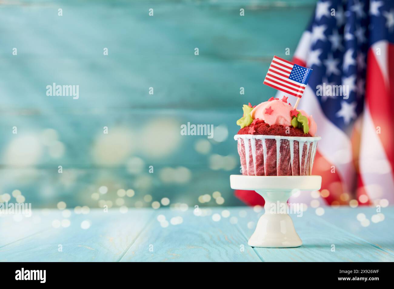 Patriotischer Cupcake 4. juli mit amerikanischer Flagge. Köstlicher Cupcake mit Frischkäse, blauem, rotem Stern auf altem blauem hölzernem Hintergrund mit Lichtern bo Stockfoto