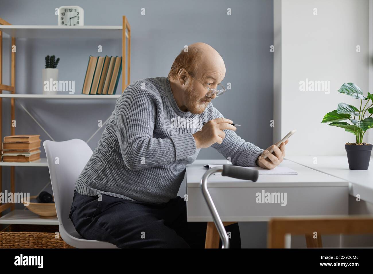 Konzentrierter Senior-Mann, der auf den Bildschirm des Smartphones blickt und Notizen auf Papier macht Stockfoto