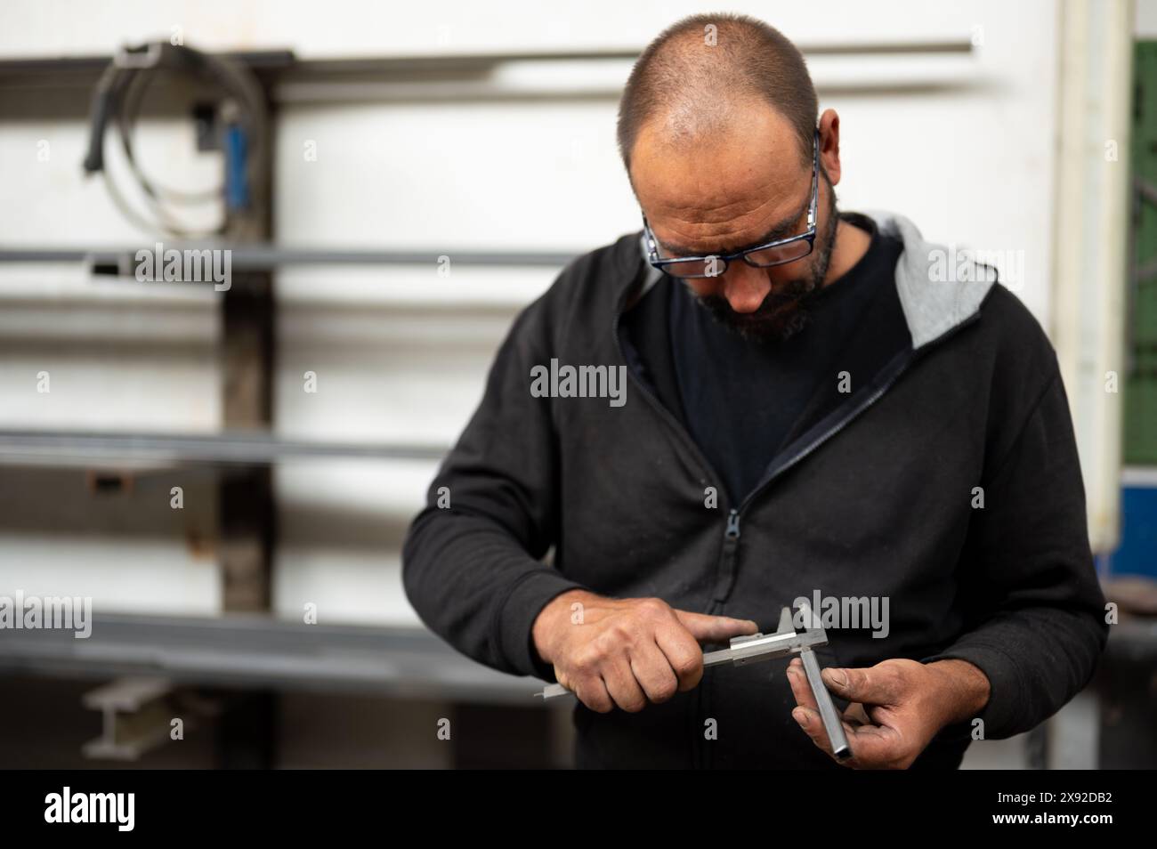 Konzeptionelle Fotografie über Metallarbeiten: Der Schmied misst eine Metallstange mit Hilfe eines Messschiebers. Konzept des Denkens bei der Arbeit, Const Stockfoto