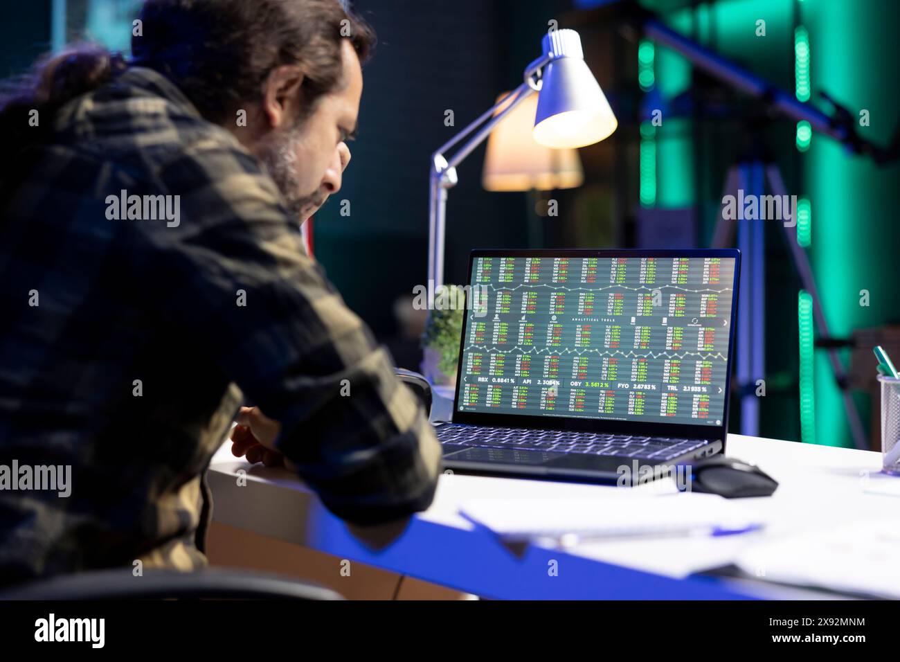 Ein ernster Mann sitzt am Schreibtisch und sieht sich die Lagerinformationen auf seinem Laptop genau an. Männlicher Freelancer konzentrierte sich auf seinen Gerätescreen, zeigte Forex-Trading-Chart an und analysierte den wirtschaftlichen Trendwert. Stockfoto