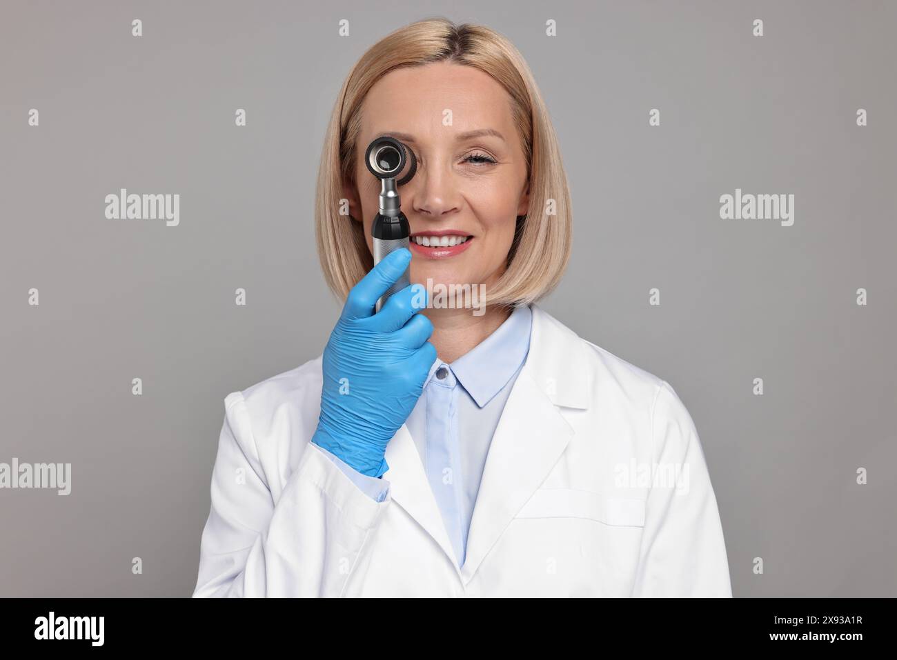 Glücklicher Dermatologe mit Dermatoskop auf grauem Hintergrund Stockfoto