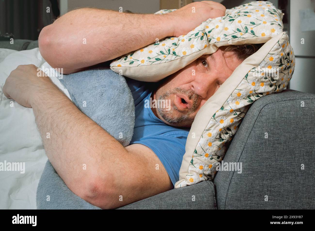 Ein Mann bedeckt sich mit Kissen und versucht zu schlafen. Lautes Geräusch, das den Schlaf stört. Keine beruhigende Gewissheit Stockfoto