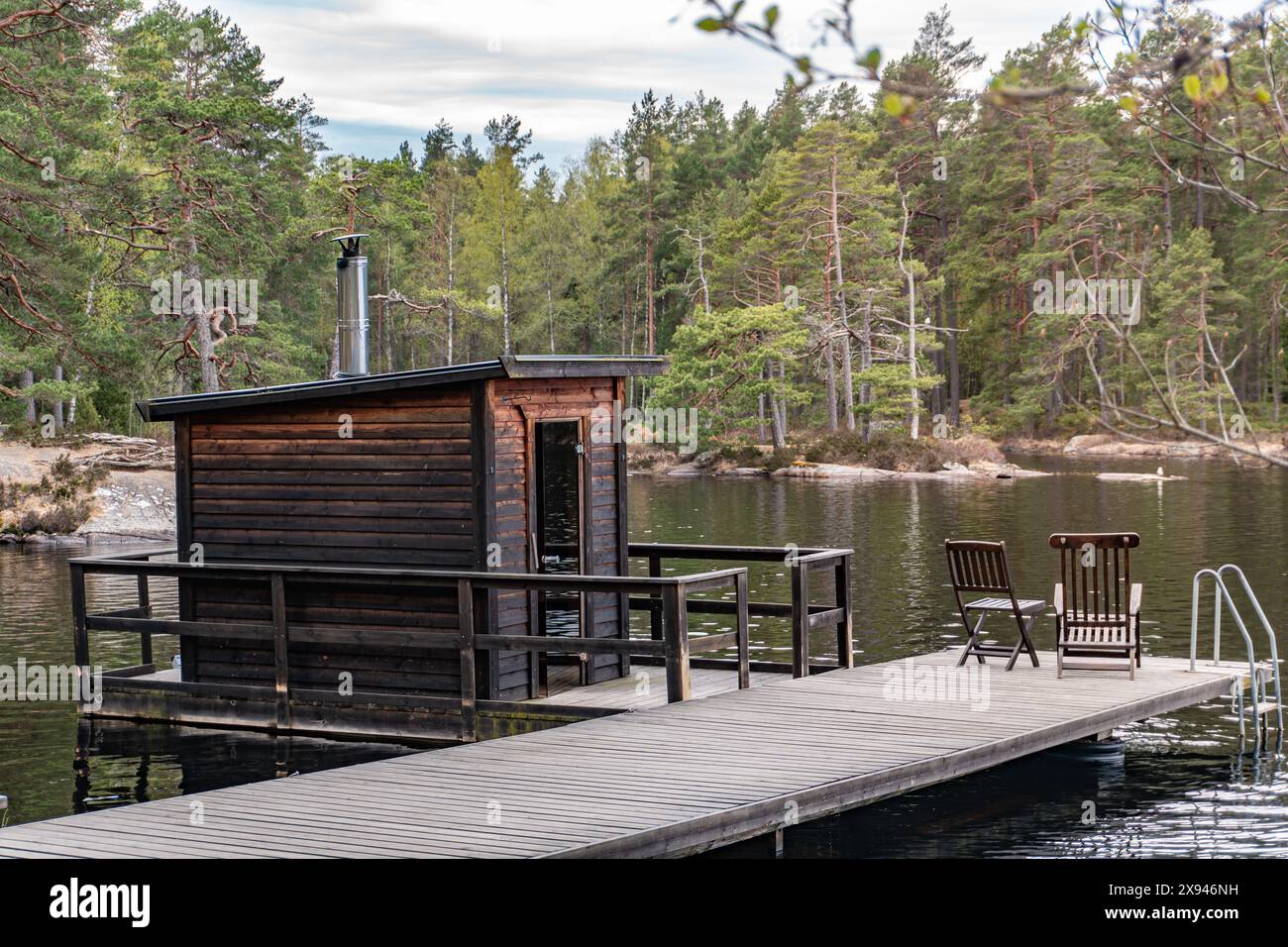 Eine Sauna am See mit Holzterrasse, die die ruhige und entspannende Atmosphäre eines Naturrefugiums einnimmt. Stockfoto