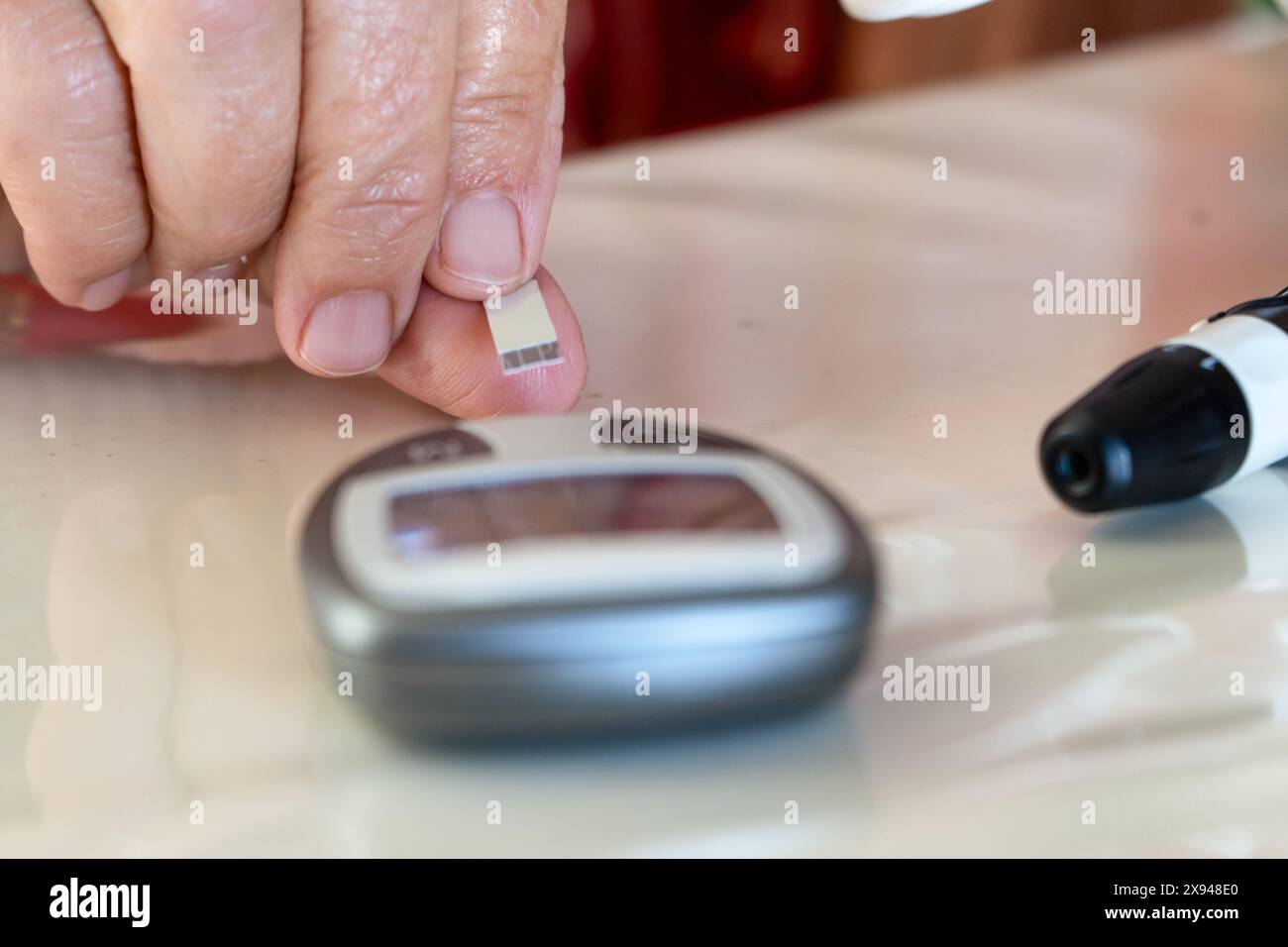 Nahaufnahme der Hand Einführen des Teststreifens auf den Zuckermonitor, um den Blutzuckerspiegel zu überprüfen Stockfoto