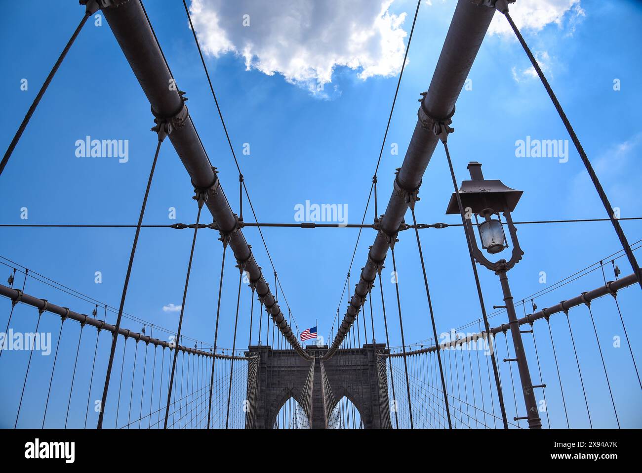 Das komplizierte Netzwerk von Hängekabeln der Brooklyn Bridge mit der amerikanischen Flagge auf einem der Türme - Manhattan, New York City Stockfoto