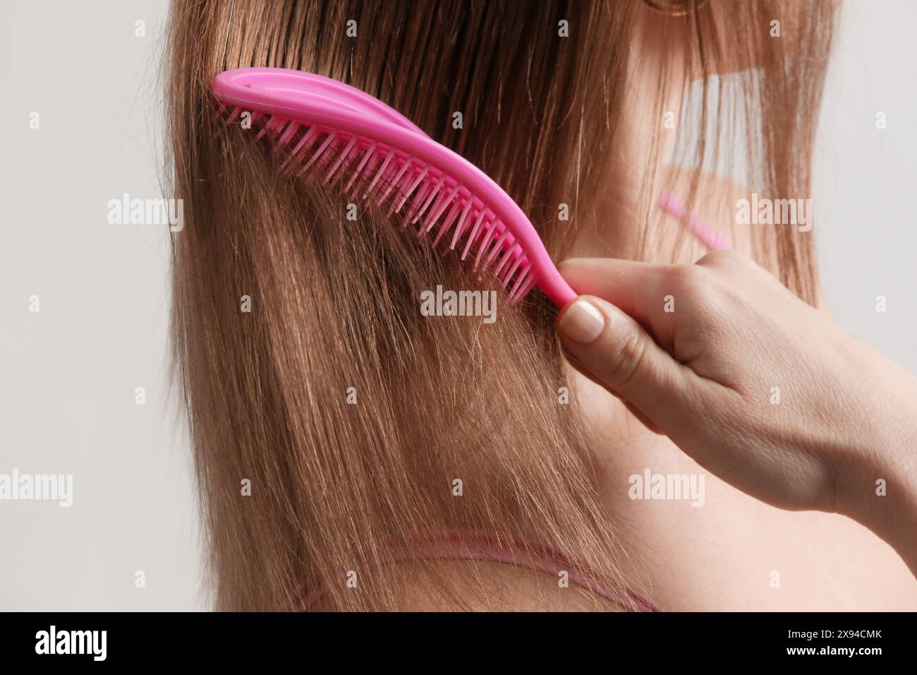 Rückansicht einer brünetten Frau, die ihr Haar mit rosa Plastik entwirrenden Haarbürste kämmt. Stockfoto