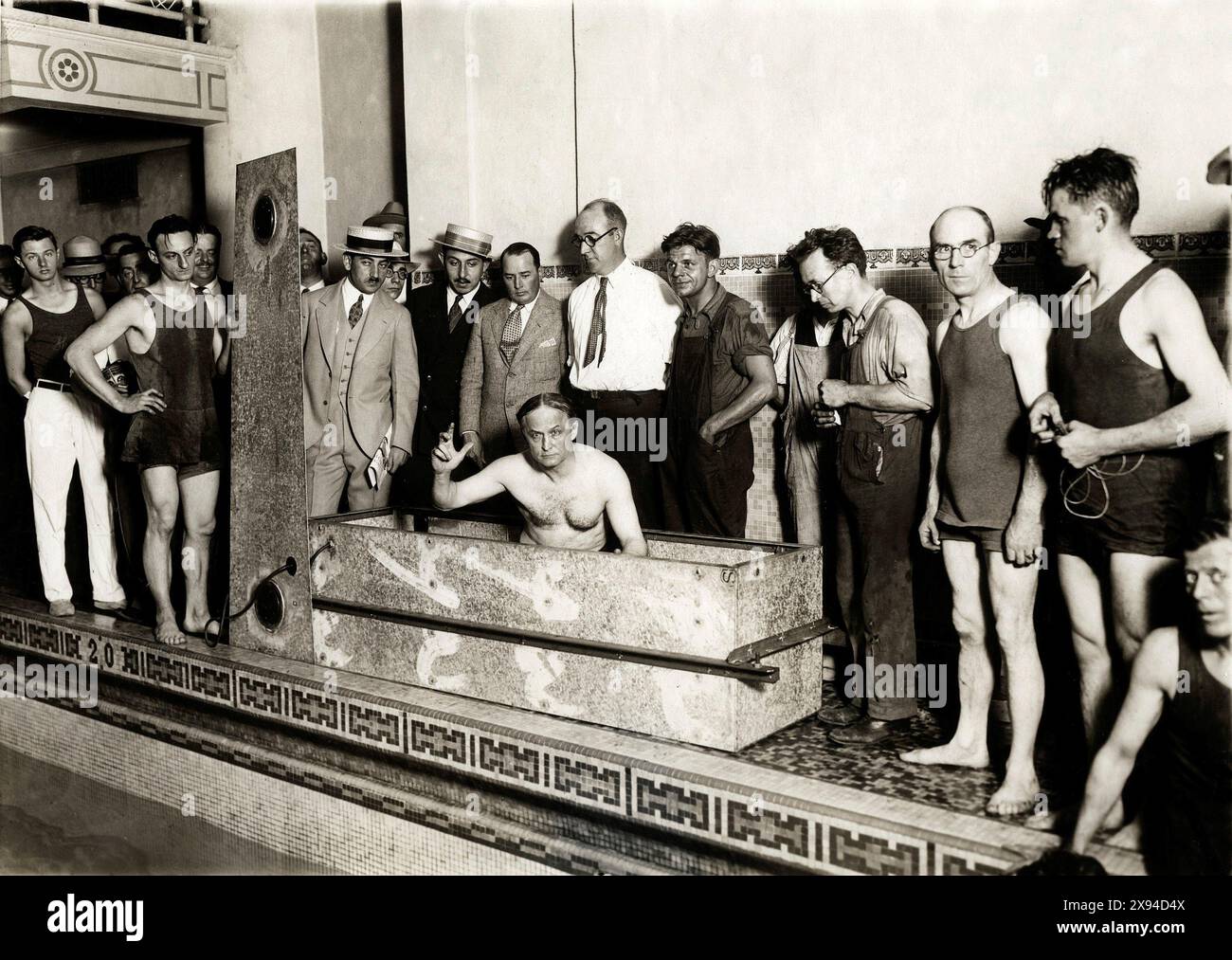 Harry Houdini in einer Stahlkiste, in der er gerade anderthalb Stunden unter Wasser verbracht hat. Am Rand des Pools beobachten eine Gruppe von Männern, mit oder ohne Badeanzüge. New York, 1926 Stockfoto