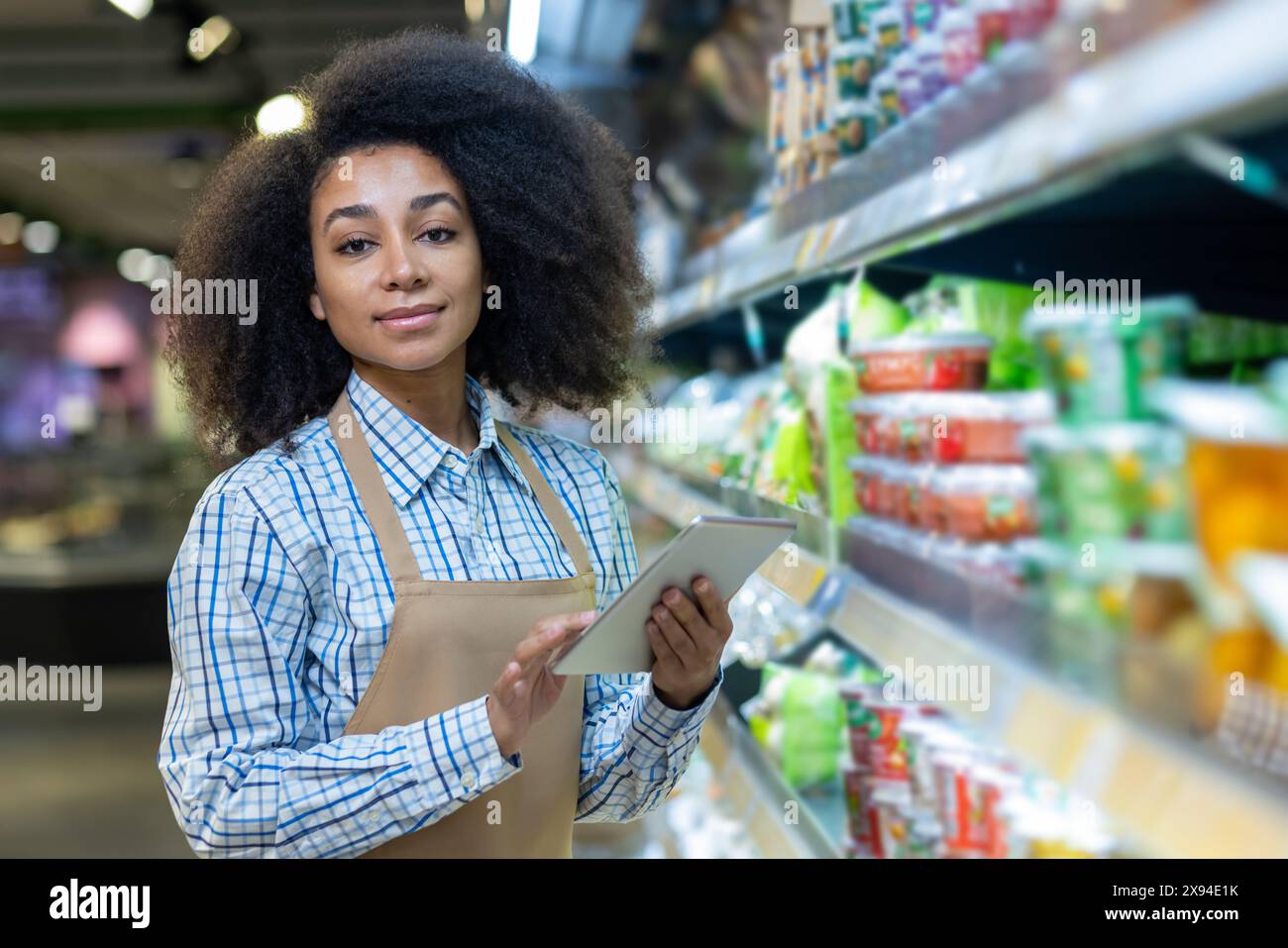 Ein Supermarktmitarbeiter mit einem Tablet in der Hand, der die Produkte in den Regalen des Gangs bearbeitet und verwaltet. Stockfoto