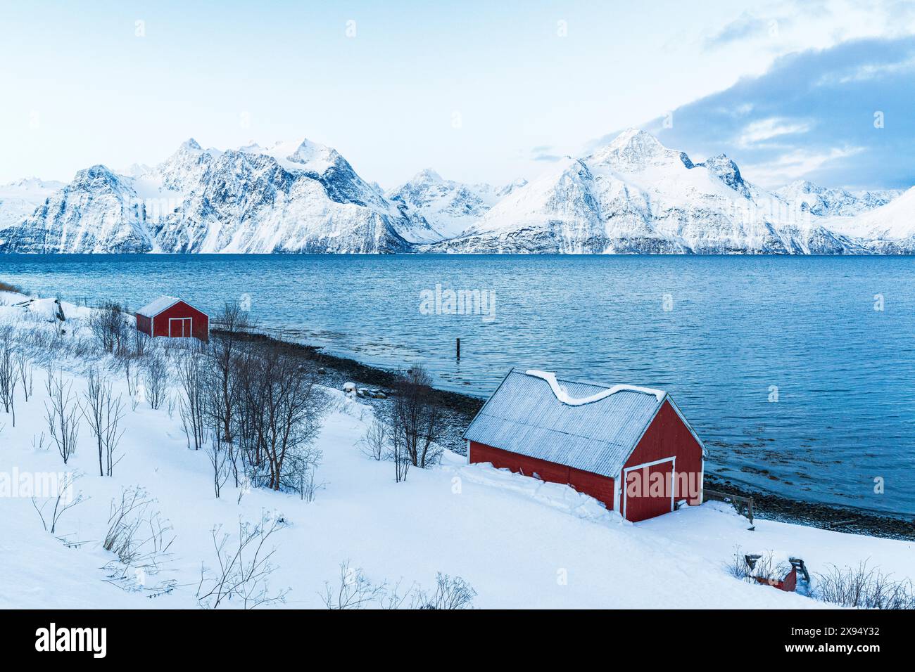 Erhöhter Blick auf den typischen roten Rorbu am Ufer des Fjords, umgeben von schneebedeckten Gipfeln am Morgen, Djupvik, Olderdalen, Lyngen Fjord, Norwegen Stockfoto