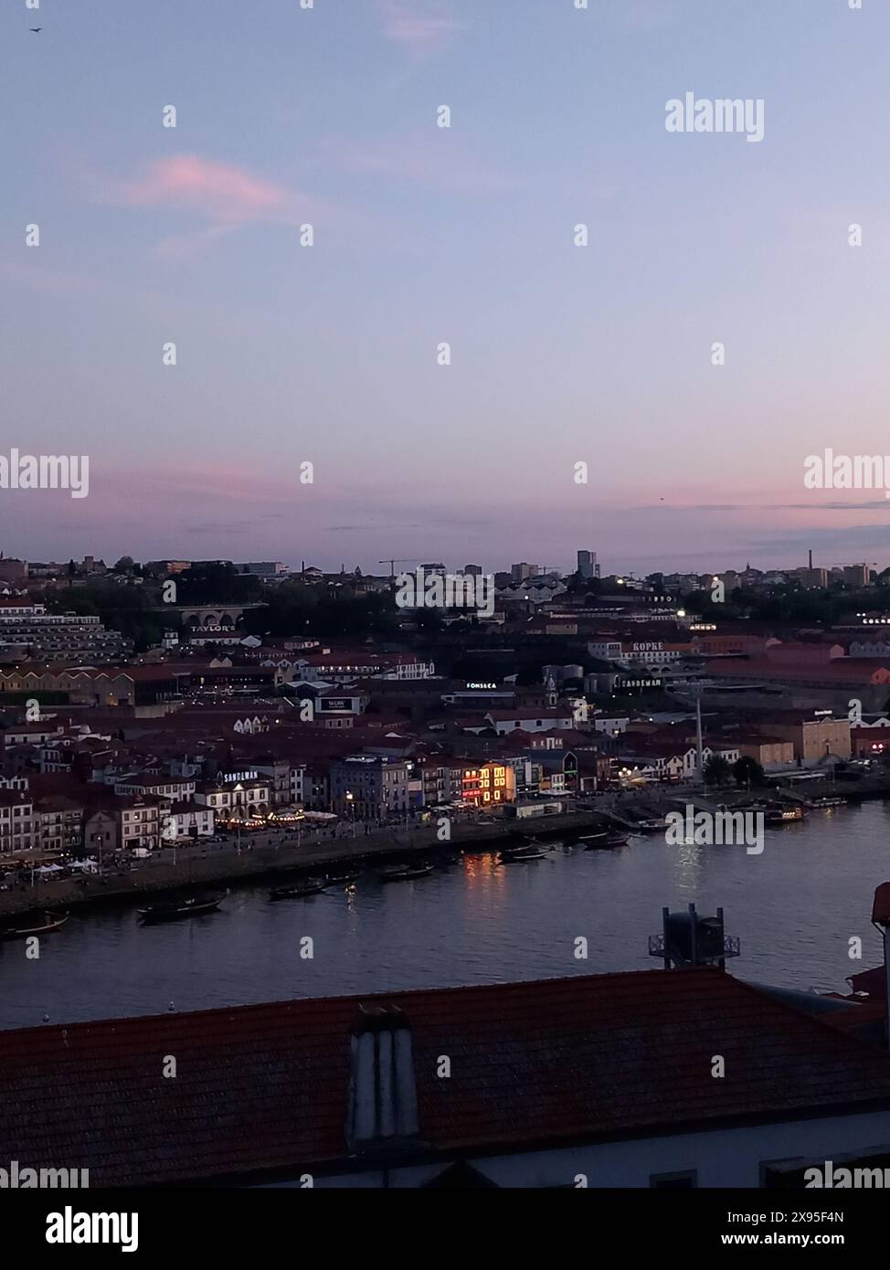 Malerischer abendlicher Blick auf eine Stadt am Fluss mit beleuchteten Gebäuden, die sich im ruhigen Wasser unter einem pastellfarbenen Himmel spiegeln Stockfoto