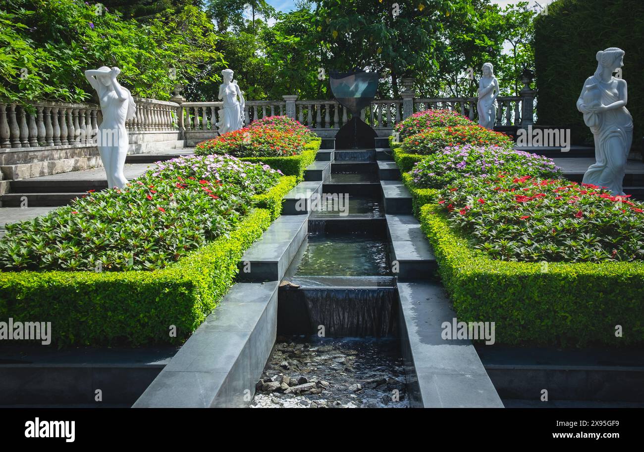 Wunderschön gestalteter Blumengarten mit Blumen, Pflanzen, griechischen Frauenstatuen mit Brunnen. Griechischer Garten Stockfoto